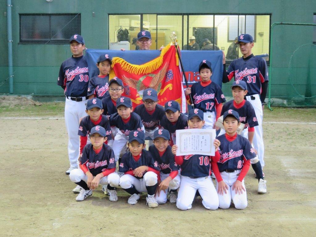 チーム旗と優勝旗を背後に賞状を持ち正面を向く優勝チーム(豊玉小ジュニア)メンバーの写真