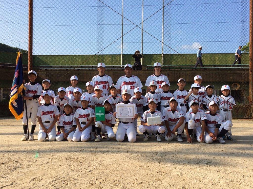 優勝旗を掲げ賞状と記念品を手に正面を向く優勝チーム(厳原少年クラブ)メンバーの写真
