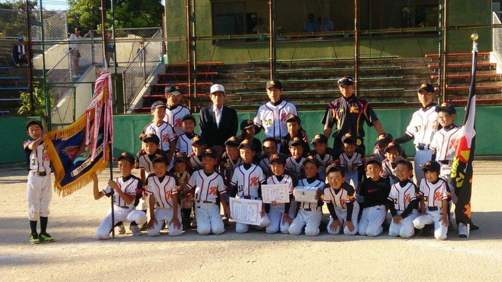 チーム旗と優勝旗を掲げ賞状と記念品を手に正面を向く優勝チーム(雞鳴ボーイズ)メンバーの写真