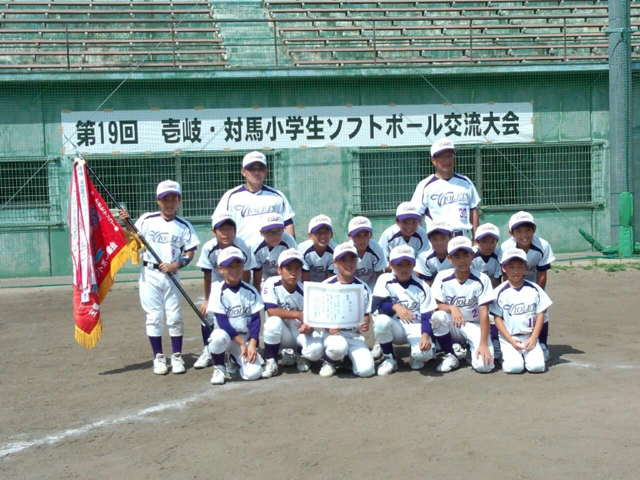 賞状と優勝旗を手に正面を向くBパート優勝チーム（上対馬バイオレッツ）メンバーの写真