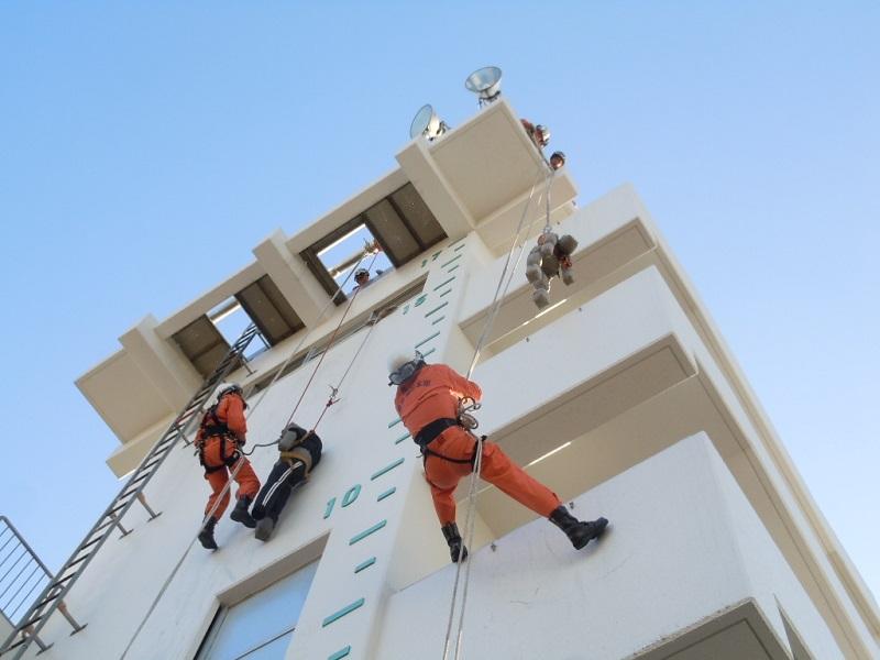 ロープでビルを昇り降りしダミー人形を使用した救助訓練を行う隊員たちの写真